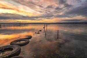 Beautiful sunset on the lake with fishing net in water and old tires photo