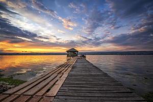 Exciting colorful long exposure landscape on a lake with a wooden pier and small house in the end. photo