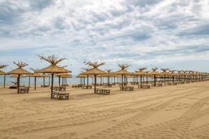 hermosas sombrillas de madera y tumbonas en una fila de playa de arena vacía foto