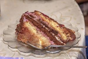 Close view of a delicate piece of chocolate cake, torte with nuts and fruits on a plate with a spoon. photo