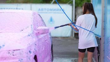 Young woman washing car with a pink foam video