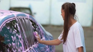 Young woman washing car with a pink foam video