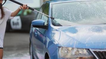 Young woman washing car with a pink foam video