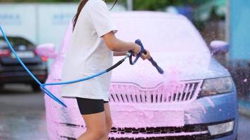 Young woman washing car with a pink foam video