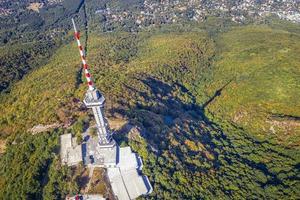 Aerial top view at a broadcasting tower on a mountain hill and city. A communications concept. photo