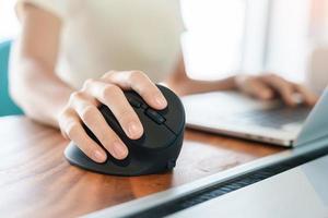 mano de mujer usando un mouse ergonómico de computadora, prevención del dolor de muñeca porque trabaja mucho tiempo. tenosinovitis de de quervain, síntoma de intersección, síndrome del túnel carpiano o concepto de síndrome de oficina foto