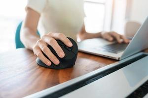 mano de mujer usando un mouse ergonómico de computadora, prevención del dolor de muñeca porque trabaja mucho tiempo. tenosinovitis de de quervain, síntoma de intersección, síndrome del túnel carpiano o concepto de síndrome de oficina foto