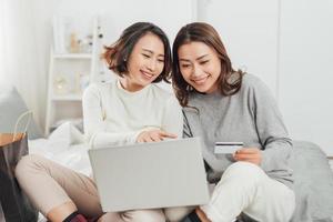 Two excited women shopping online with credit card and laptop at home photo