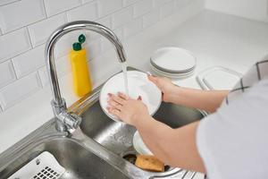 manos de mujer enjuagando platos con agua corriente en el fregadero foto