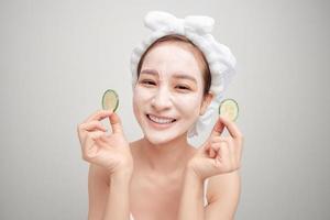 Young woman with clay facial mask holding cucumber slices isolated on white background photo