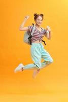smiling young woman or student with backpack jumping in air over yellow background photo