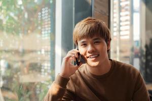 joven seguro de sí mismo hablando por teléfono móvil y sonriendo mientras está sentado en el café foto