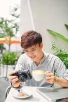 Portrait of good-looking guy holding photo camera while sitting at the table with cup of coffee