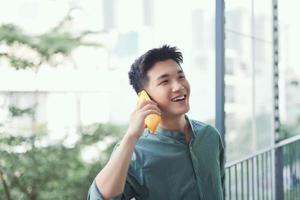 hombre asiático hablando por teléfono inteligente sonriendo riendo a carcajadas relajándose en el balcón foto