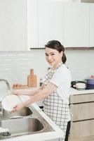 bella joven sonriente lavando los platos en la moderna cocina blanca. foto