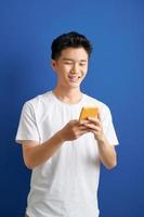 Smiling young good looking Asian man using smartphone to get in touch with family and friends isolated on blue  background photo