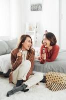 Cheerful young female friend with brush as mic singing while sitting on the bedwhile resting on bed during makeup photo