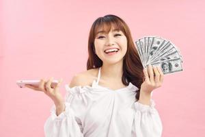 Image of a beautiful excited young woman posing isolated over pink wall background holding money and using mobile phone. photo