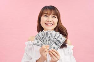 Image of delighted woman wearing basic clothes smiling and holding money cash isolated over pink background photo