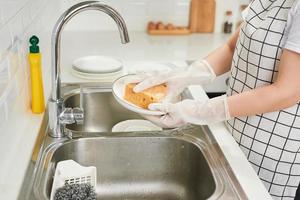 Kitchen porter cleaning white plates in sink in professional kitchen photo