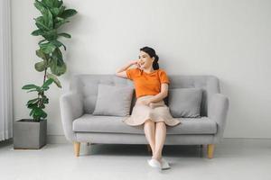 Peaceful young woman with hands behind head relaxing on cozy sofa at home photo