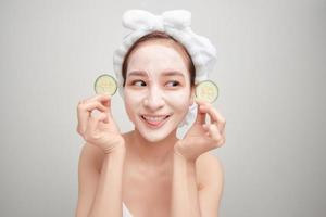 Beautiful girl holding a slice of cucumber in front of her face with mask of clay. photo