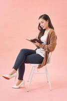 Happy young woman is sitting in a chair thinking about something, writing everything in a notebook photo