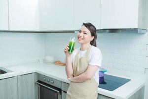 Woman drinking green detox juice, smoothie drink in kitchen portrait. photo