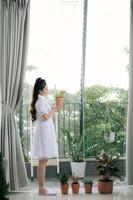 Asian smiling woman holding and looking at tree in the planted pot. Concept idea of planting trees as a happy hobby. photo