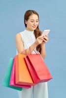 Making the retail connection. Beautiful young woman with shopping bags using her smart phone with smile while standing photo