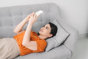 Attractive woman smiling as she reads an sms message on her mobile while relaxing on a sofa photo