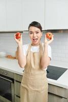 attractive funny house wife lady arms holding two big tomato playful mood enjoy morning cooking tasty dinner wait family guests wear apron stand modern kitchen indoors