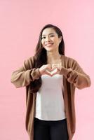 Young woman standing isolated on pink background showing heart shape hand gesture looking camera smiling cheerful photo