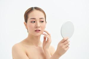 Young Asian woman with problem face looking at the mirror  over white background. photo