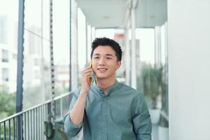 Young handsome man having conversation on smartphone at balcony at sunny summer day photo