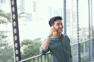 Happy man speaking on cellphone standing on balcony in city in summer day photo