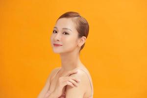Charming woman touching her perfect soft face skin with fingers, smiling at camera over yellow background photo