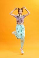 Young beautiful energy girl with white headphones listening to music laughs and jump on yellow background photo