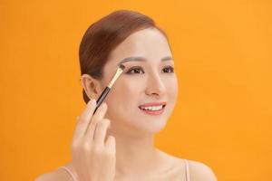 Beautiful woman using brush for eyeshadow. Photo of woman with perfect makeup on yellow background. Beauty concept