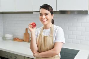 Asian women wear apron posing in the kitchen at home looking at camera, red apple in hand photo