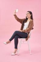 una joven sonriente haciendo una foto selfie en un smartphone con un fondo rosa