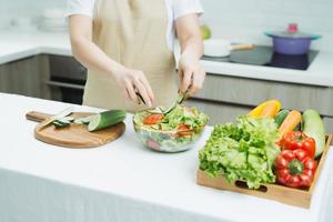 Smiling young woman in apron stand in modern kitchen preparing salad photo