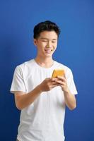 Smiling young good looking Asian man using smartphone to get in touch with family and friends isolated on blue  background photo