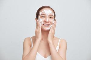 Portrait of cheerful laughing woman applying foam for washing on her face. photo