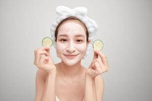 Beautiful girl holding a slice of cucumber in front of her face with mask of clay. photo
