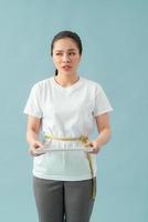 A asian woman holding scales with a tape measure around her belly on a blue background photo