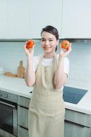 Cheery girl holding in hands tomato cooking everyday in modern light white interior kitchen photo