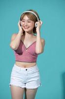 Upbeat positive Asian girl enjoys every bit of music wears stereo headphones on her ears holds a mobile phone listens to favorite audio track photo