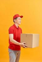 Cheerful delivery man. Happy young courier holding a cardboard box and smiling while standing against white background photo