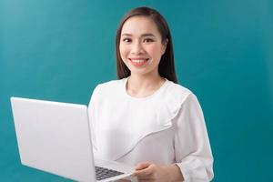 Image of cheerful young woman standing isolated over blue background using laptop computer. Looking camera. photo